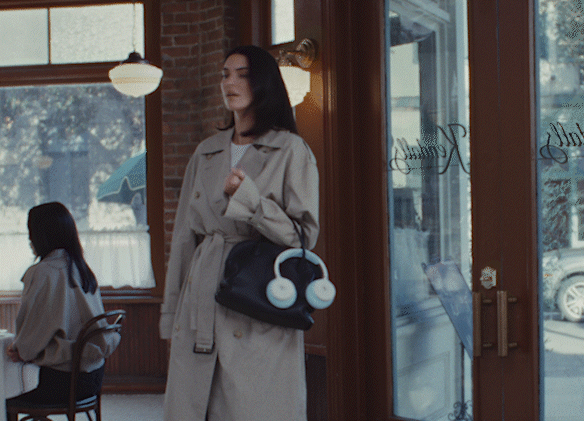 Kendall Jenner waving inside of a cafe with Beats 360 headphones hanging over her purse.